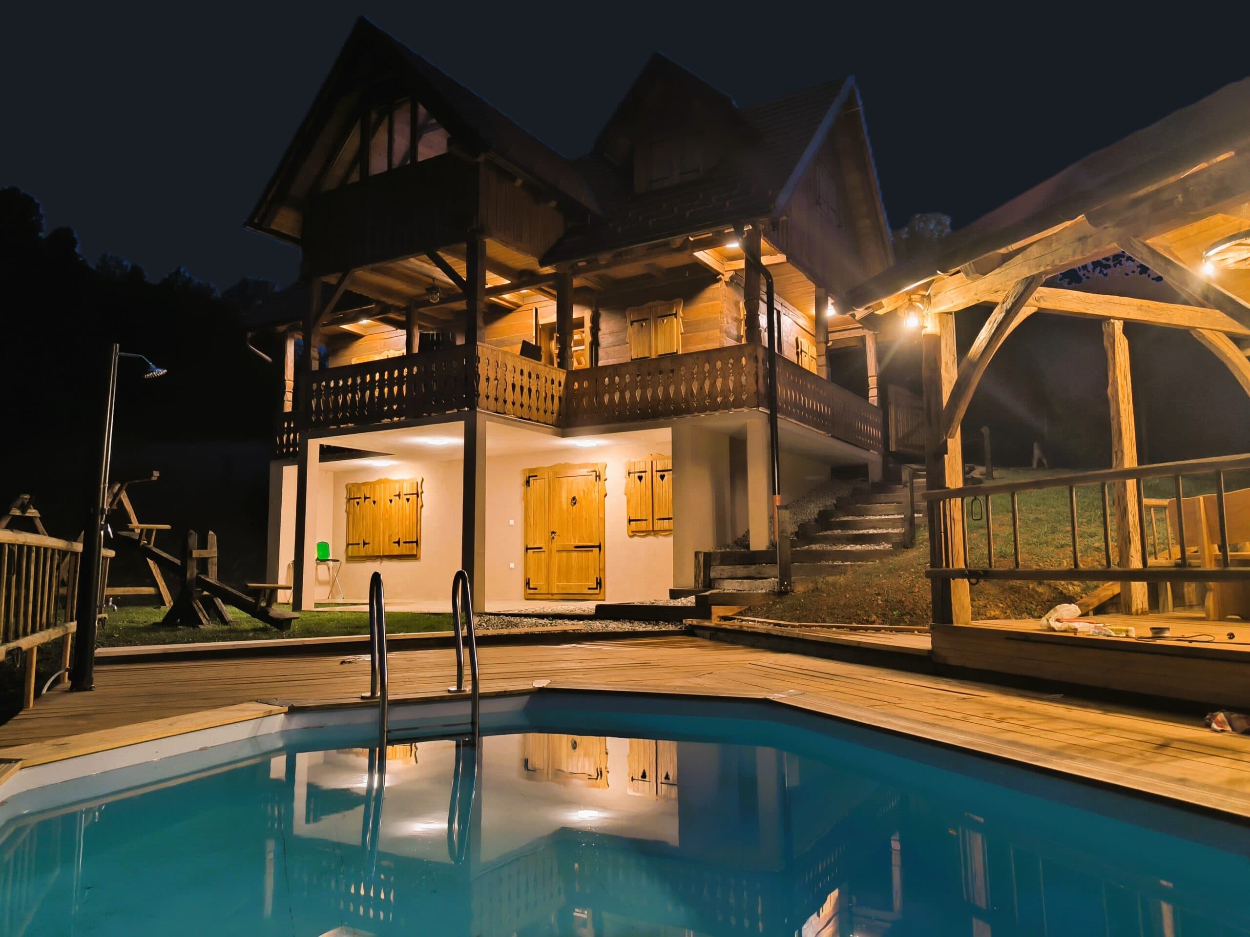 Oak House Mrežnica illuminated at night, its pool reflecting the warm glow of the wooden cabin