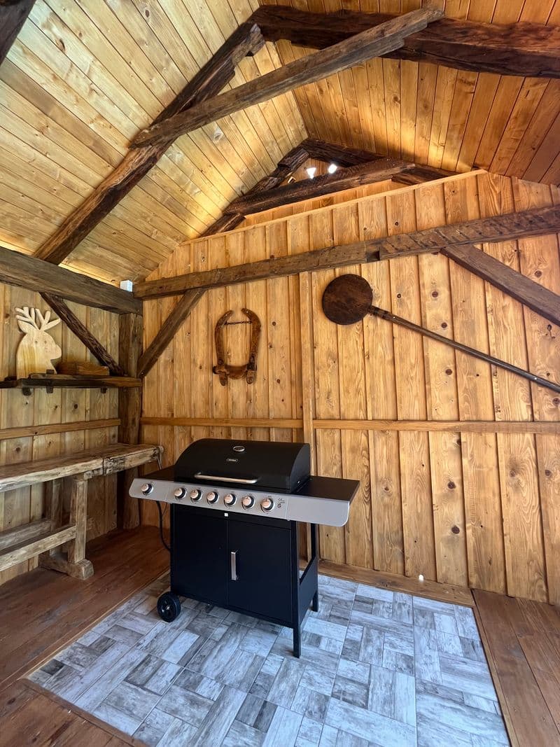 Rustic outdoor kitchen with a gas grill under a timber roof