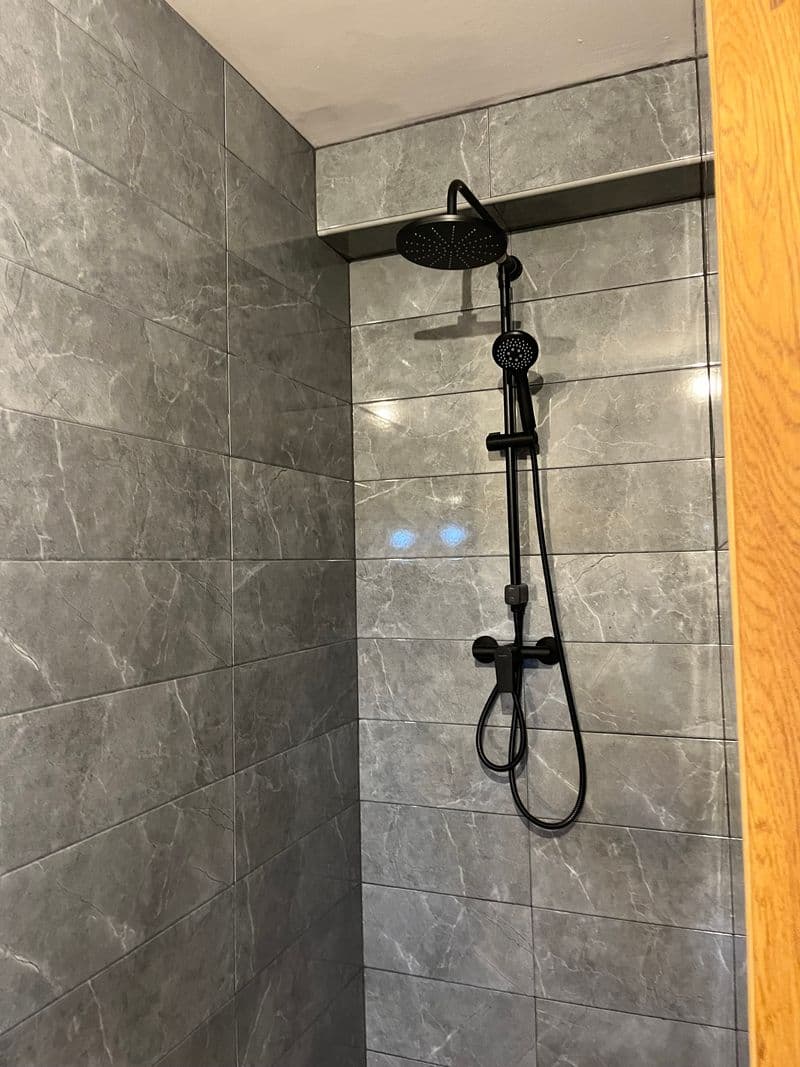 Walk-in rain shower with dark fixtures and marble-effect tiling