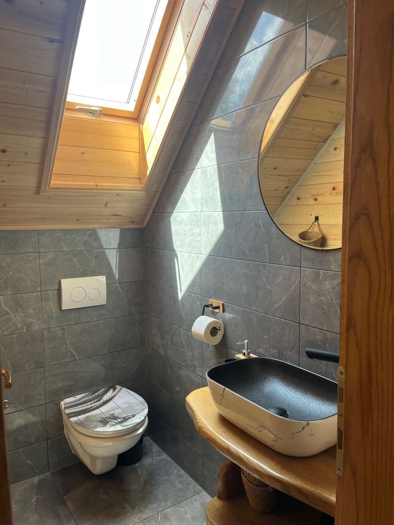 Modern bathroom with grey stone tiles, round mirror and skylight