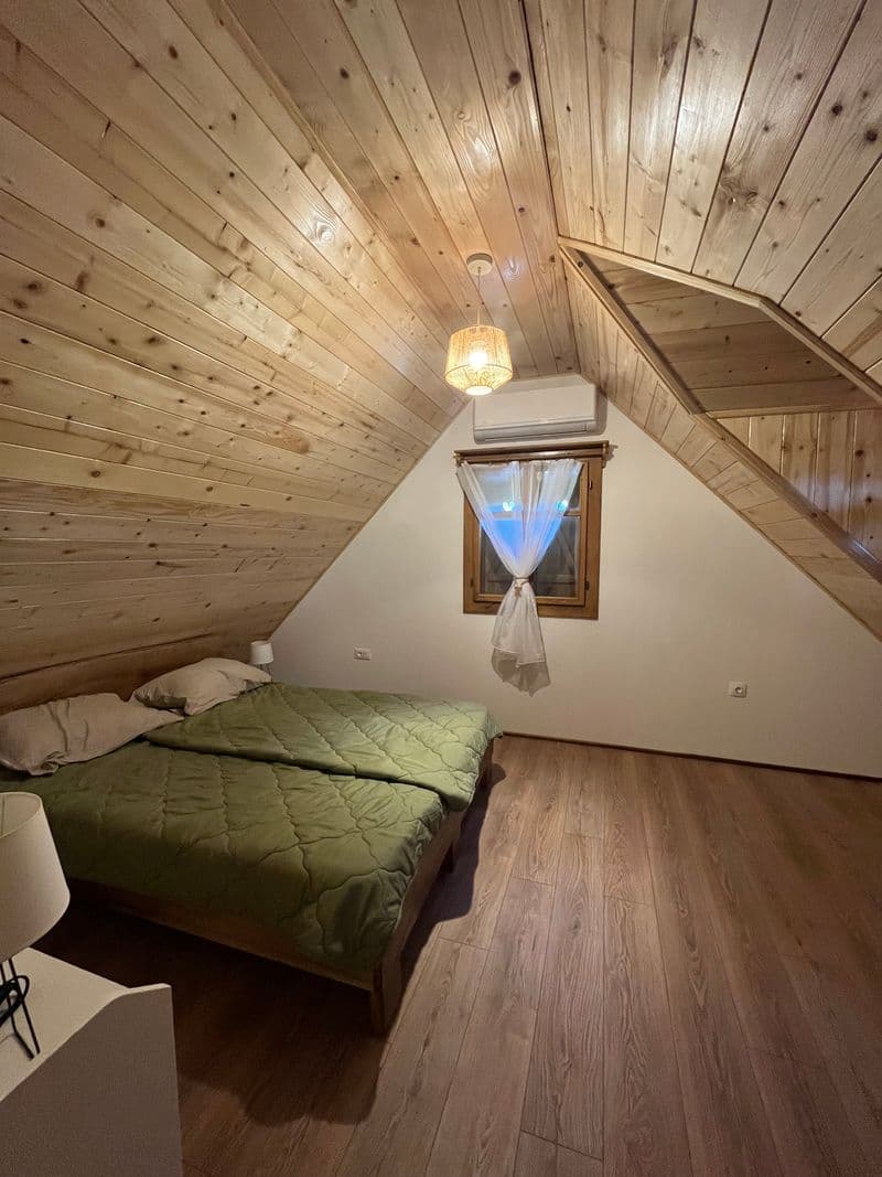 Double bedroom under the pitched wooden roof with a window and air conditioning