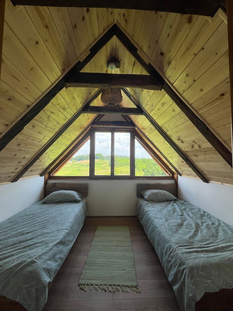 Twin room in the A-frame gable with a triangular window framing the countryside